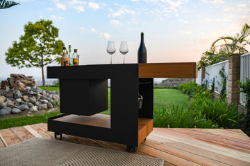 A captivating lifestyle image of the Indu+ Bar Isle placed outdoors with a picturesque mini waterfall in the background. The bar isle is adorned with two elegant wine glasses and a selection of spirits, creating a sophisticated and inviting setting for outdoor entertaining.