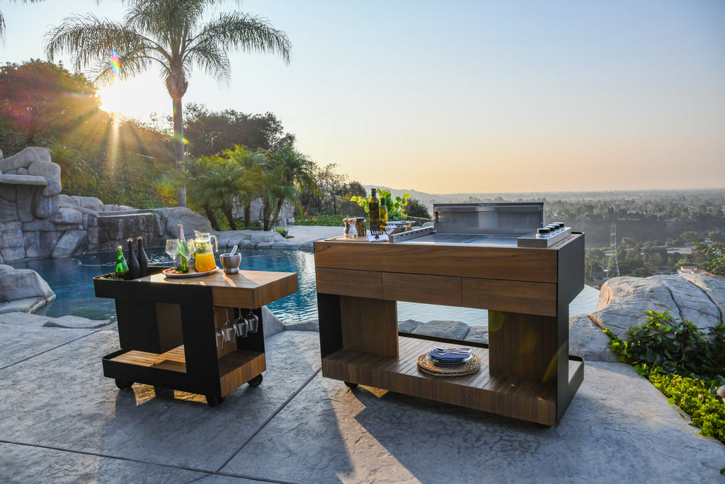 Scenic lifestyle image showcasing the Indu+ Bar Isle and Bistro Island by the pool, with a breathtaking city view in the background. The Bar Isle exudes elegance with its sophisticated setup of glasses, beverages, and a stylish serving area. The Bistro Island complements the scene with its chic design and enticing culinary possibilities. Enjoy a luxurious outdoor experience with these captivating islands against the stunning cityscape backdrop.